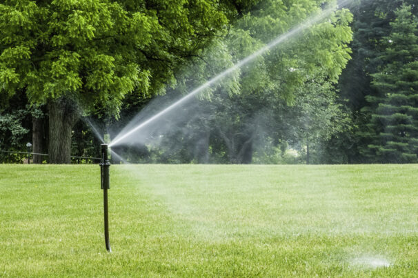 Tall sprinkler spraying lawn with long jet of water on college campus